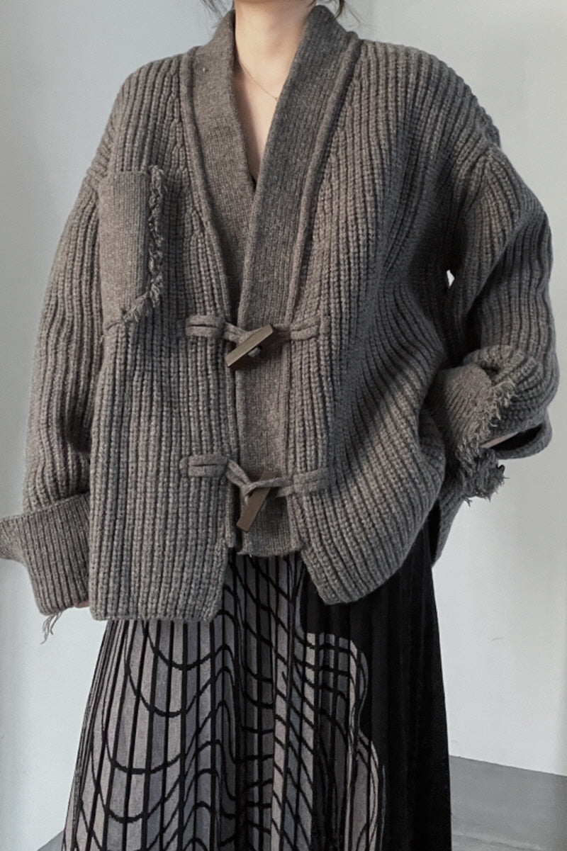 Cozy gray knit cardigan with toggle closures, styled with a flowy skirt, showcasing modern winter fashion from Belle Vestige.